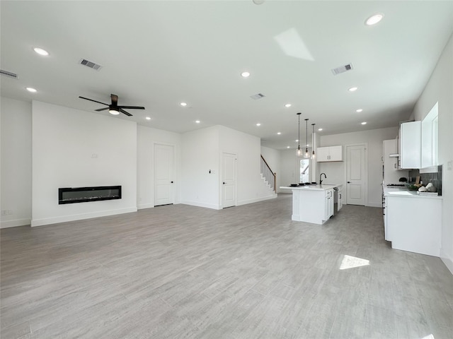 unfurnished living room featuring light wood-type flooring, sink, and ceiling fan