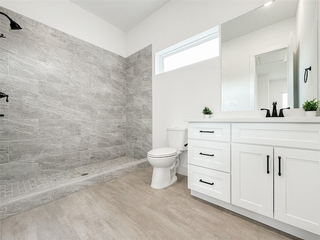 bathroom featuring vanity, hardwood / wood-style flooring, toilet, and a tile shower