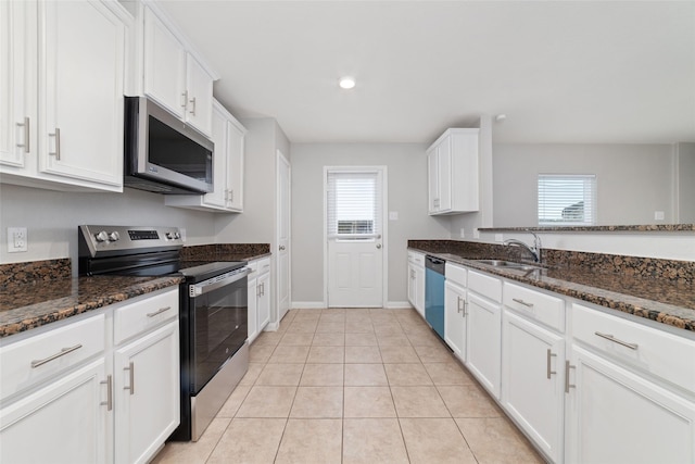 kitchen featuring sink, appliances with stainless steel finishes, white cabinetry, dark stone countertops, and light tile patterned flooring