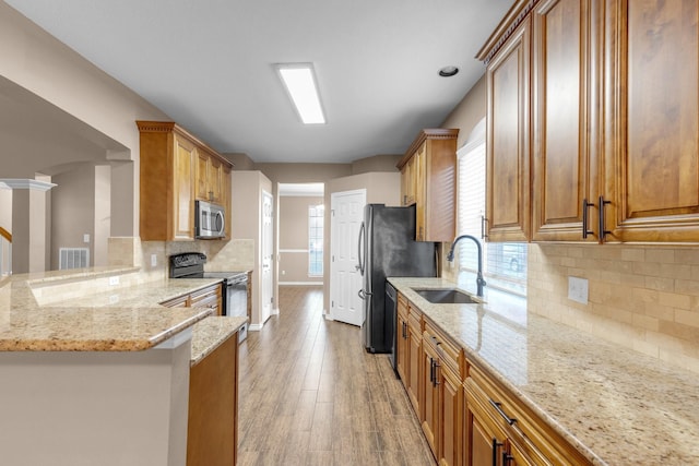 kitchen featuring sink, appliances with stainless steel finishes, light stone counters, light hardwood / wood-style floors, and kitchen peninsula