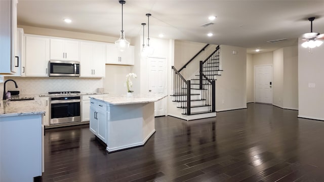 kitchen featuring sink, appliances with stainless steel finishes, a kitchen island, pendant lighting, and white cabinets