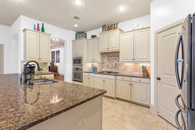 kitchen with dark stone countertops, arched walkways, stainless steel appliances, and a sink