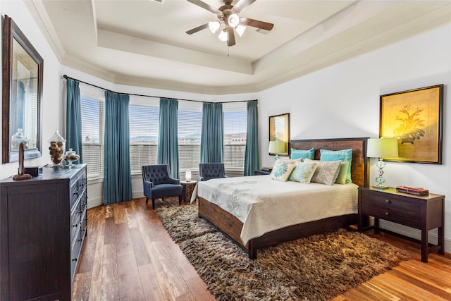 bedroom featuring a tray ceiling, ceiling fan, baseboards, and wood finished floors