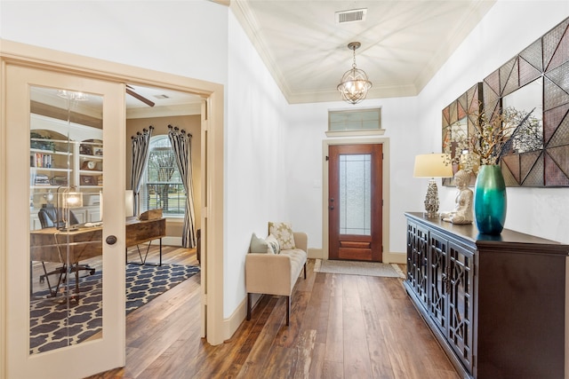 foyer featuring wood finished floors, visible vents, baseboards, ornamental molding, and an inviting chandelier