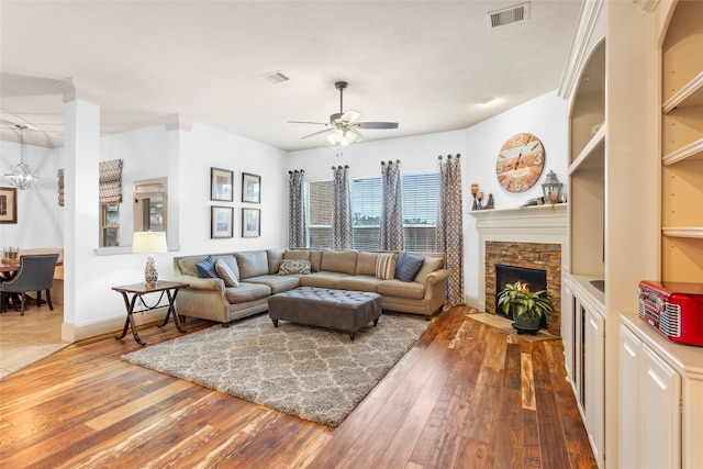 living room featuring a stone fireplace, wood finished floors, visible vents, and a ceiling fan