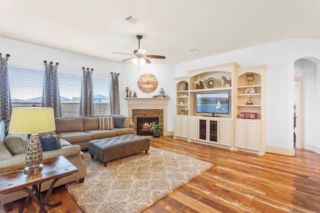 living area featuring baseboards, visible vents, arched walkways, light wood-style floors, and a fireplace