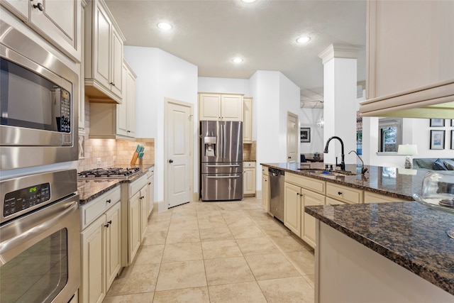 kitchen with cream cabinetry, dark stone counters, stainless steel appliances, and a sink