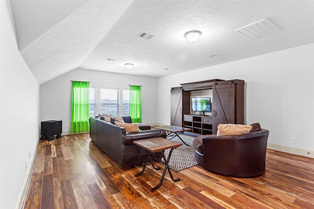 living area with a barn door, a textured ceiling, visible vents, and wood finished floors