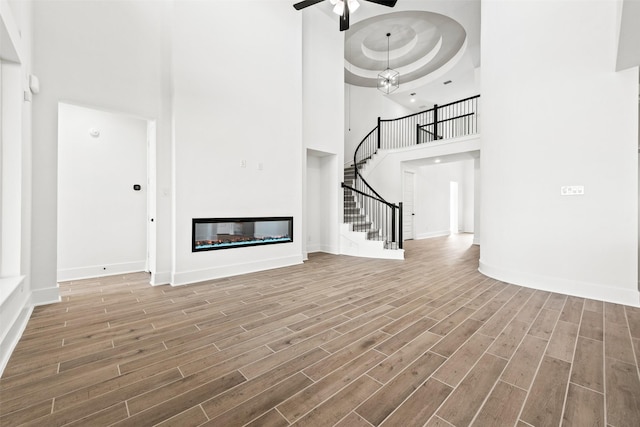 unfurnished living room with hardwood / wood-style floors, a tray ceiling, ceiling fan, and a towering ceiling