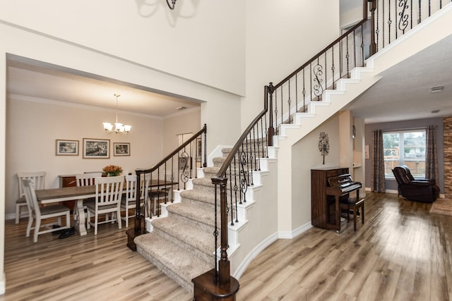 staircase with a high ceiling, wood-type flooring, ornamental molding, and a chandelier