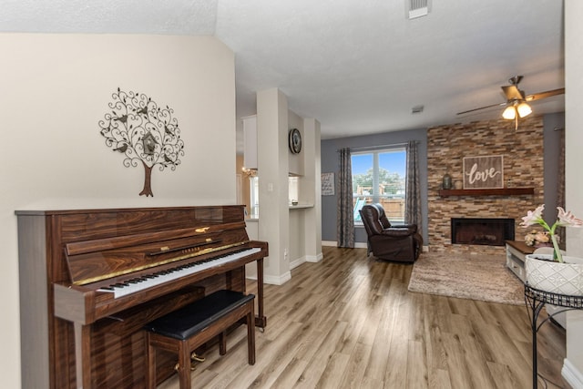 interior space featuring a stone fireplace, a textured ceiling, ceiling fan, and light wood-type flooring