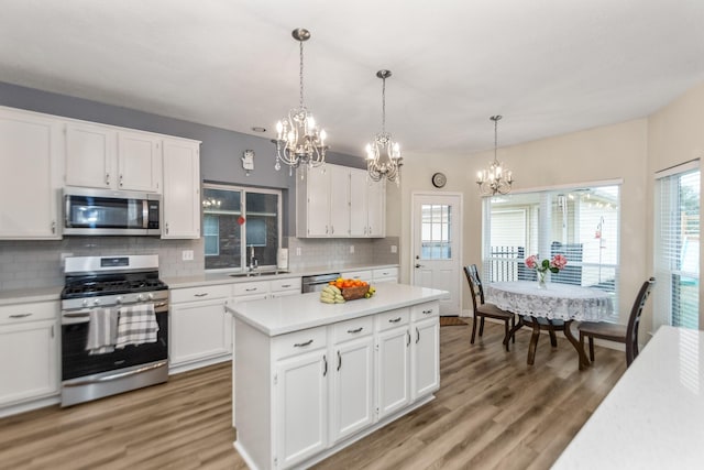 kitchen featuring tasteful backsplash, hanging light fixtures, hardwood / wood-style flooring, stainless steel appliances, and white cabinets