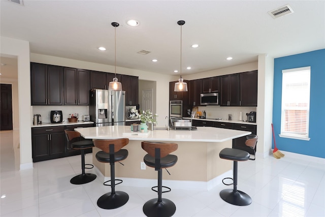 kitchen featuring pendant lighting, a breakfast bar, dark brown cabinets, stainless steel appliances, and an island with sink