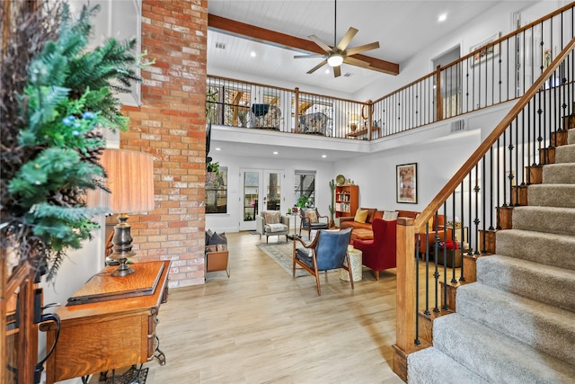 living area with wood finished floors, visible vents, a ceiling fan, stairway, and beamed ceiling