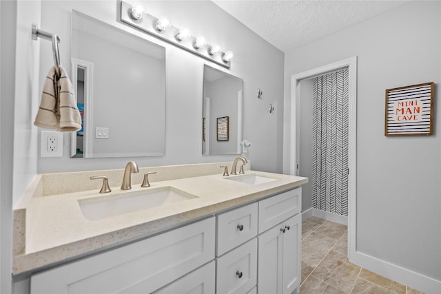 bathroom with double vanity, a textured ceiling, baseboards, and a sink