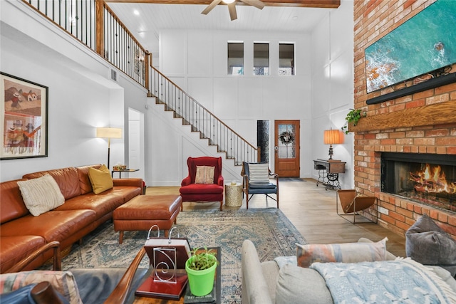 living area featuring wood finished floors, beamed ceiling, stairs, a brick fireplace, and a decorative wall