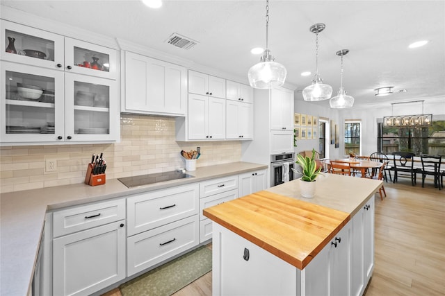 kitchen featuring black electric cooktop, visible vents, stainless steel oven, white cabinetry, and wooden counters