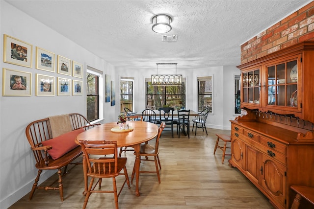 dining room with light wood-type flooring, visible vents, a textured ceiling, and baseboards