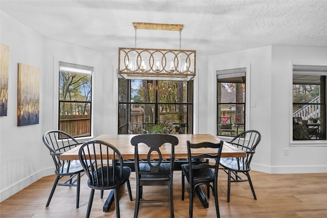 dining space featuring a textured ceiling, baseboards, a notable chandelier, and wood finished floors