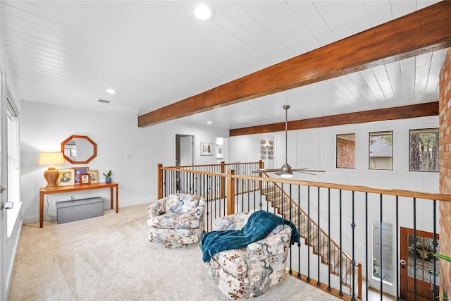 sitting room featuring beamed ceiling, plenty of natural light, carpet flooring, and an upstairs landing