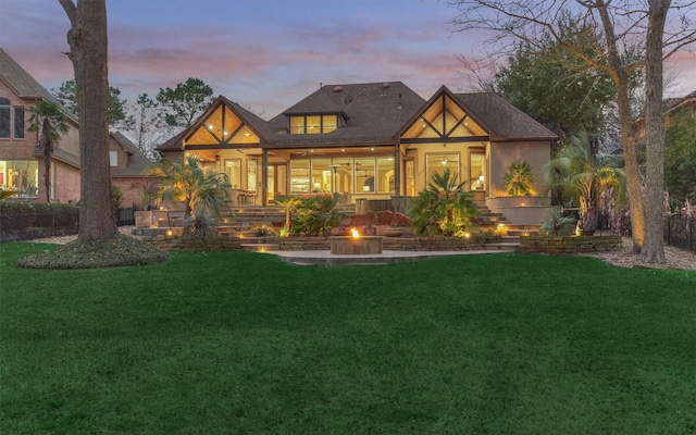 back house at dusk featuring a patio, a lawn, and a fire pit