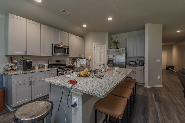 kitchen with dark hardwood / wood-style flooring, light stone countertops, an island with sink, and appliances with stainless steel finishes