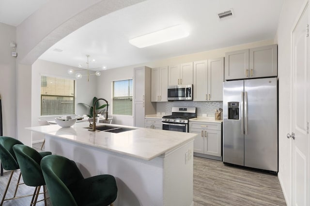 kitchen with a center island with sink, stainless steel appliances, sink, gray cabinets, and a kitchen breakfast bar