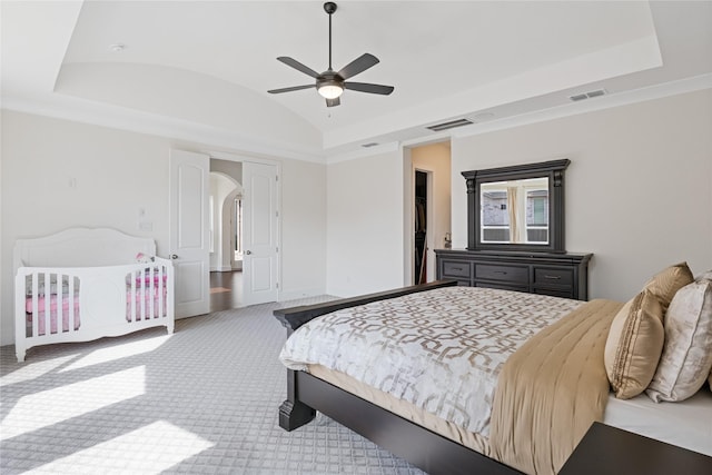 carpeted bedroom with a tray ceiling, vaulted ceiling, and ceiling fan