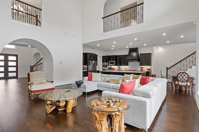 living room featuring stairs, arched walkways, a high ceiling, and dark wood finished floors