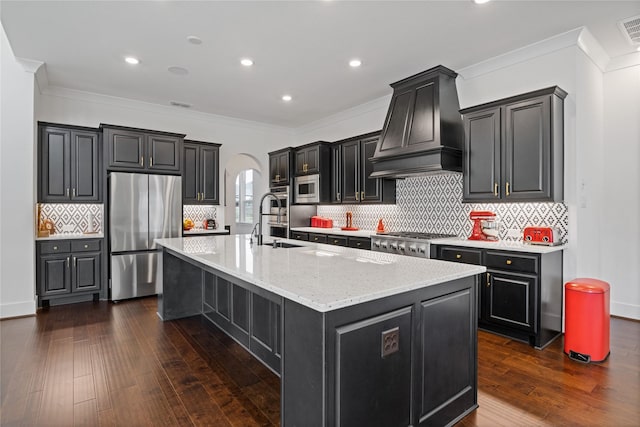 kitchen featuring a sink, dark cabinetry, arched walkways, stainless steel appliances, and custom range hood