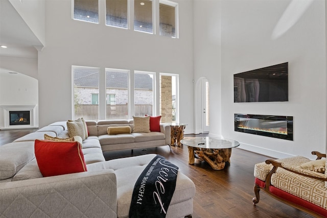 living room featuring a high ceiling, a glass covered fireplace, and wood finished floors