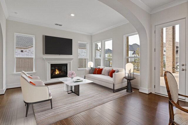 living room featuring arched walkways, visible vents, a glass covered fireplace, and ornamental molding