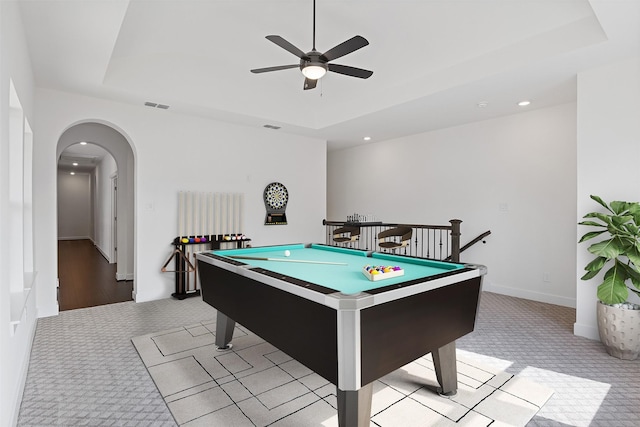 rec room with visible vents, a ceiling fan, light carpet, a tray ceiling, and arched walkways
