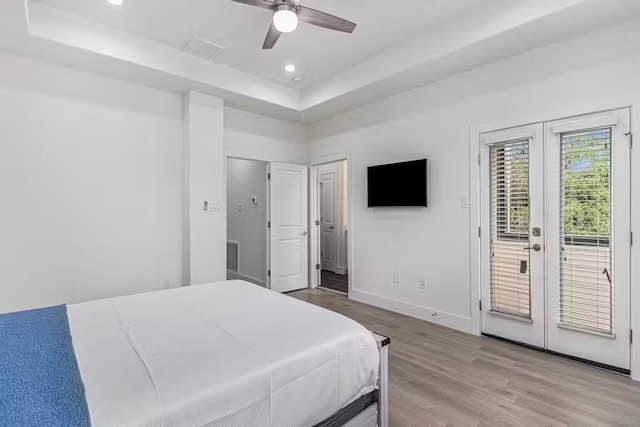 bedroom featuring french doors, light wood-type flooring, a tray ceiling, ceiling fan, and access to exterior