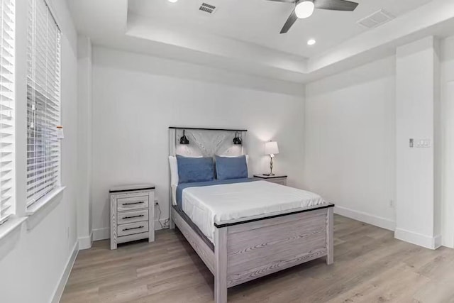 bedroom featuring a tray ceiling, ceiling fan, and light wood-type flooring