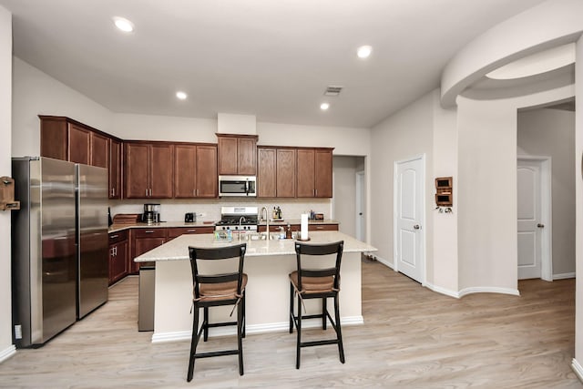 kitchen with light hardwood / wood-style flooring, a kitchen breakfast bar, stainless steel appliances, light stone countertops, and a kitchen island with sink