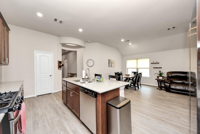 kitchen with vaulted ceiling, appliances with stainless steel finishes, an island with sink, sink, and light hardwood / wood-style flooring