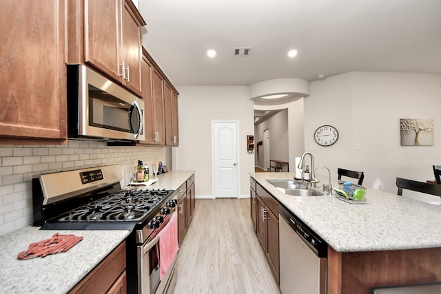 kitchen featuring a kitchen bar, sink, a center island with sink, stainless steel appliances, and backsplash