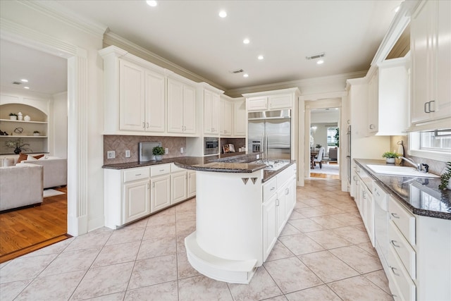 kitchen with light tile patterned floors, dark stone countertops, a center island, white cabinets, and stainless steel built in fridge