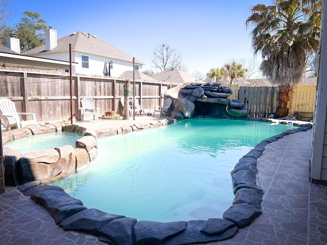 view of swimming pool featuring a water slide, a fenced backyard, and a pool with connected hot tub