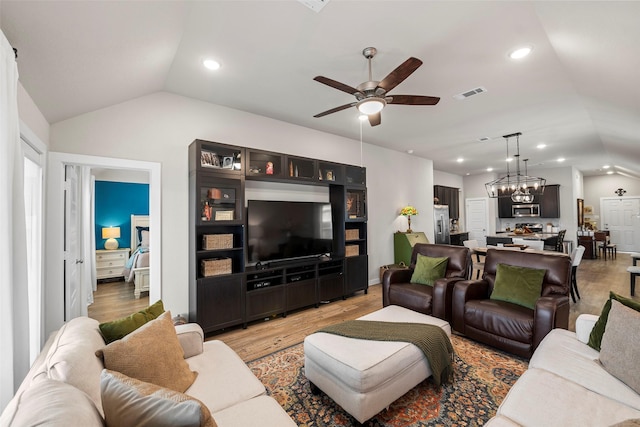 living room featuring lofted ceiling, ceiling fan with notable chandelier, and light hardwood / wood-style flooring