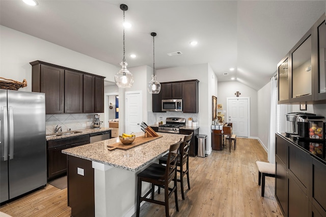 kitchen with hanging light fixtures, stainless steel appliances, a center island, dark brown cabinetry, and light stone countertops