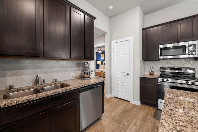 kitchen featuring sink, dark brown cabinetry, light stone counters, stainless steel appliances, and light hardwood / wood-style floors