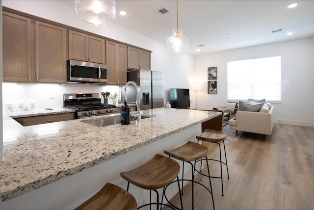 kitchen featuring stainless steel appliances, hanging light fixtures, sink, and light stone counters