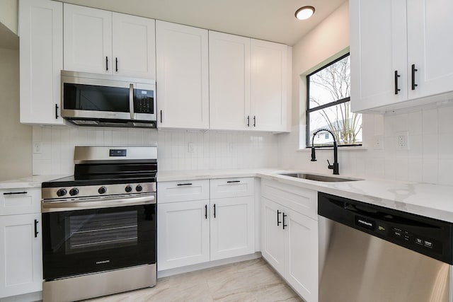 kitchen with stainless steel appliances, sink, white cabinets, and light stone counters