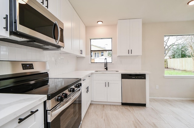 kitchen featuring stainless steel appliances, light stone countertops, sink, and white cabinets