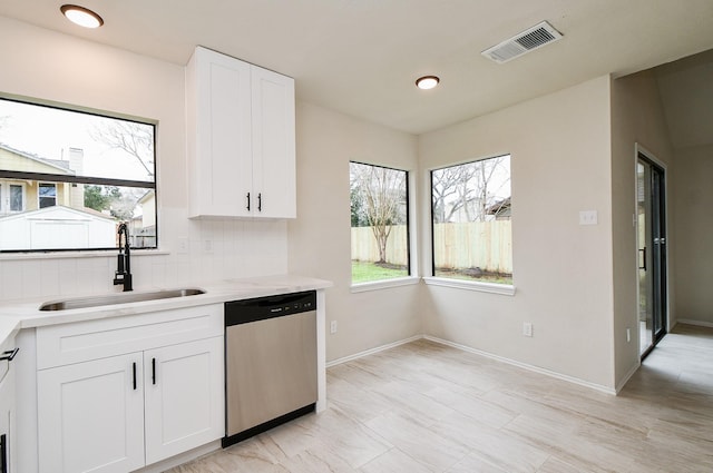 kitchen with tasteful backsplash, white cabinetry, sink, stainless steel dishwasher, and light stone countertops