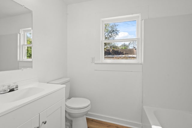 bathroom with hardwood / wood-style flooring, a tub to relax in, vanity, and toilet