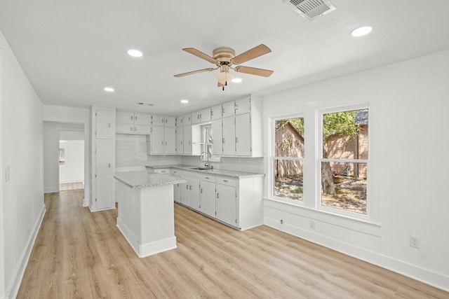 kitchen with white cabinetry, a center island, sink, and light hardwood / wood-style flooring