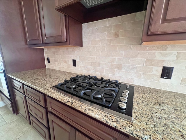 kitchen featuring wall chimney exhaust hood, light stone countertops, stainless steel gas cooktop, and decorative backsplash